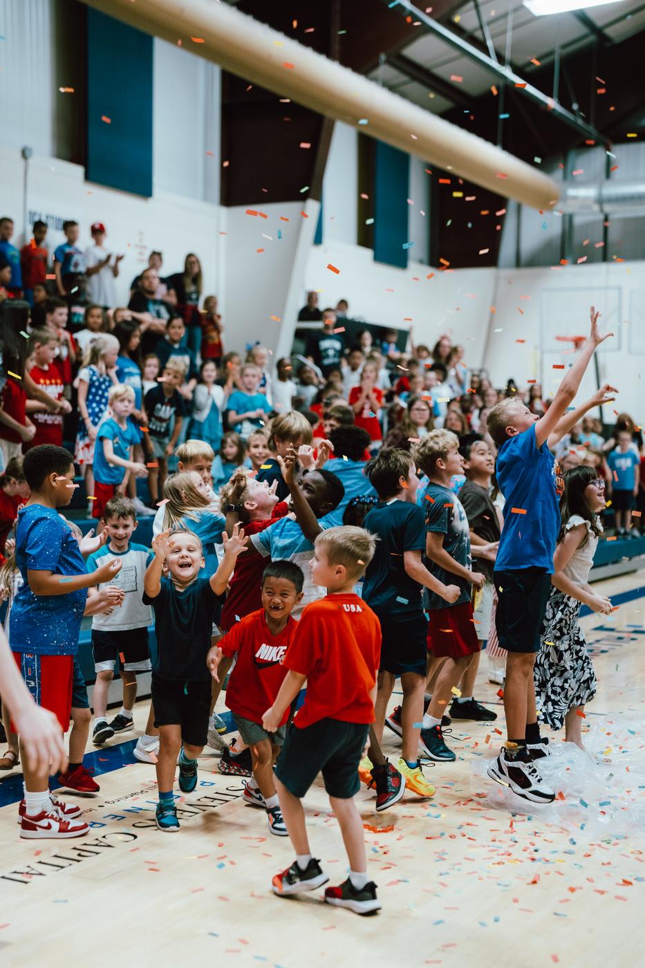 Students cheering and jumping as confetti falls in the school gym
