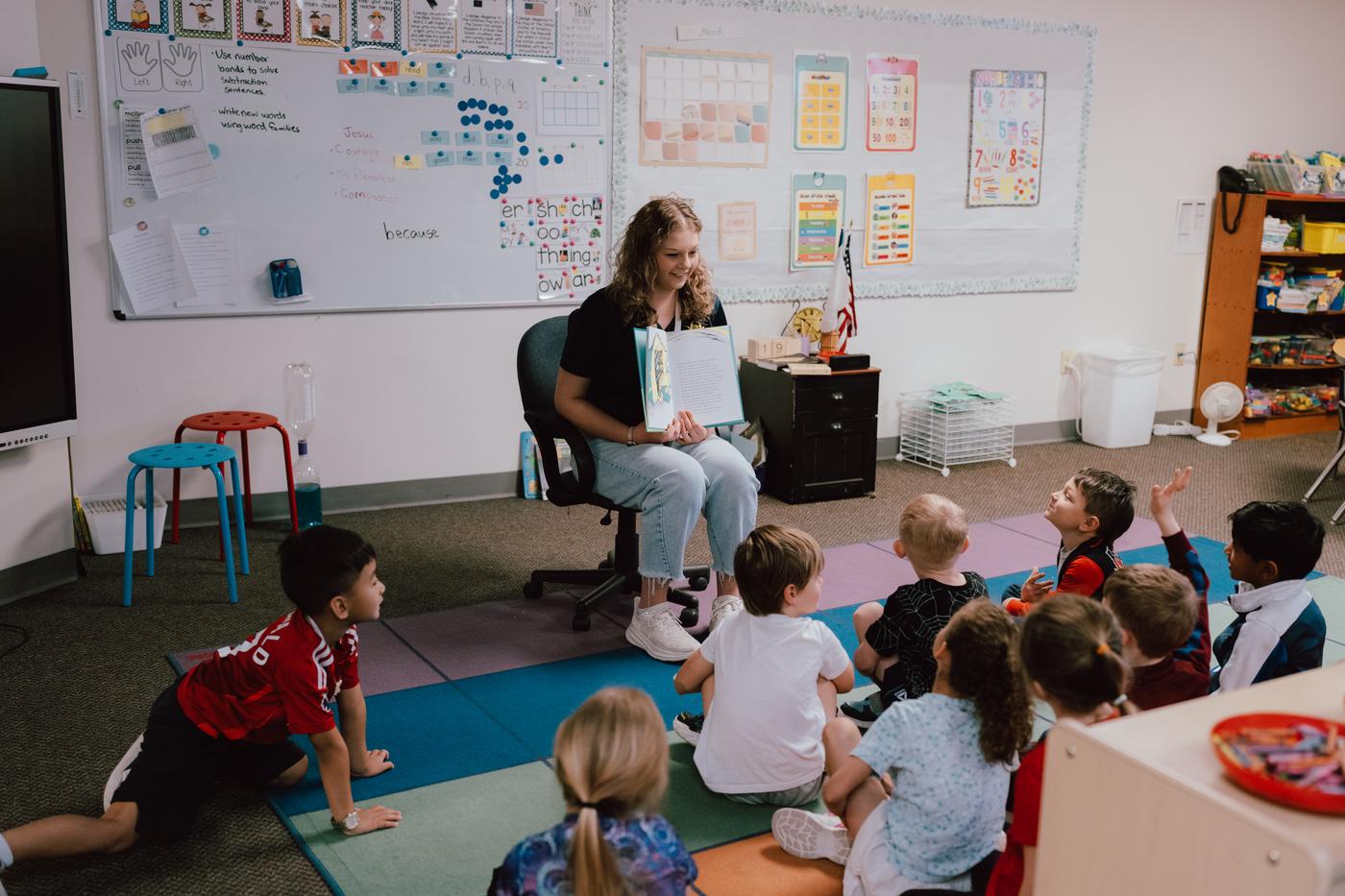 A teacher reading to young students gathered on a classroom rug