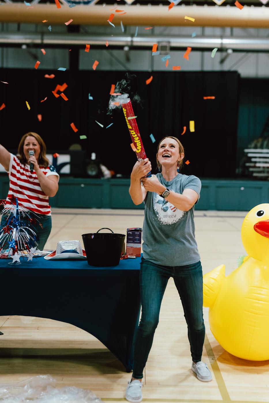 A teacher popping a confetti cannon during a school celebration in the gym
